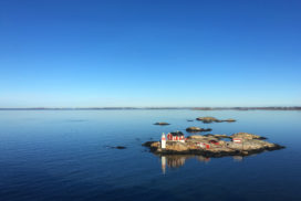 Øy ved kysten av Sverige, blå himmel, blått rolig vann, rødt hus og en liten fyrlykt, veldig rolig bilde