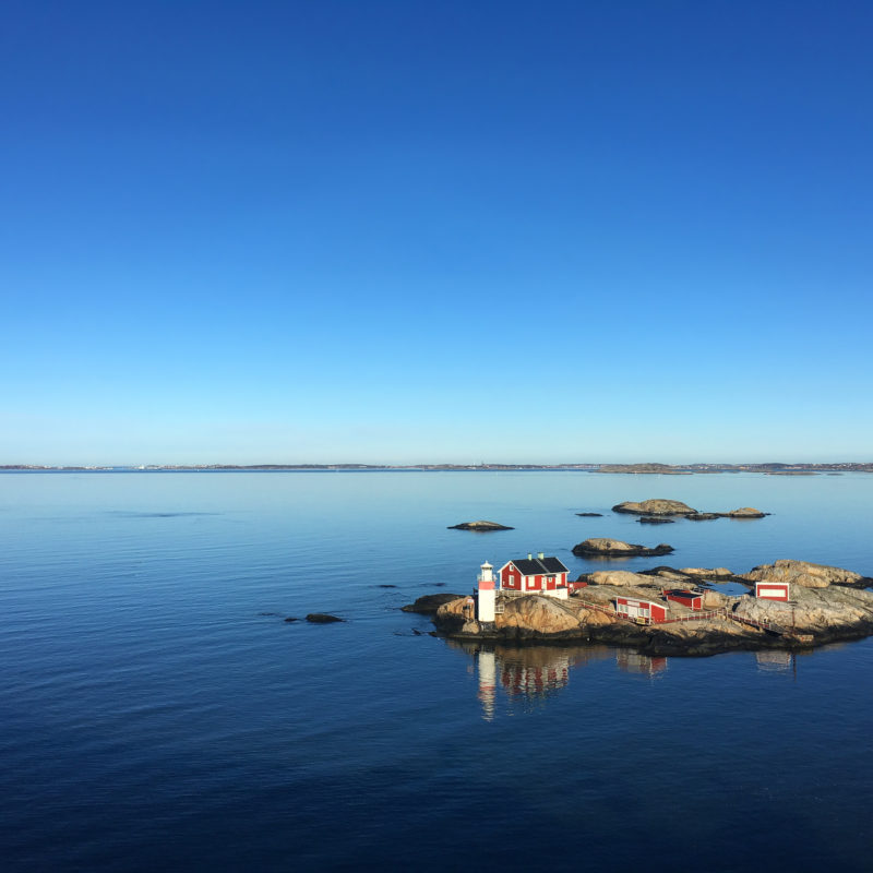 Øy ved kysten av Sverige, blå himmel, blått rolig vann, rødt hus og en liten fyrlykt, veldig rolig bilde